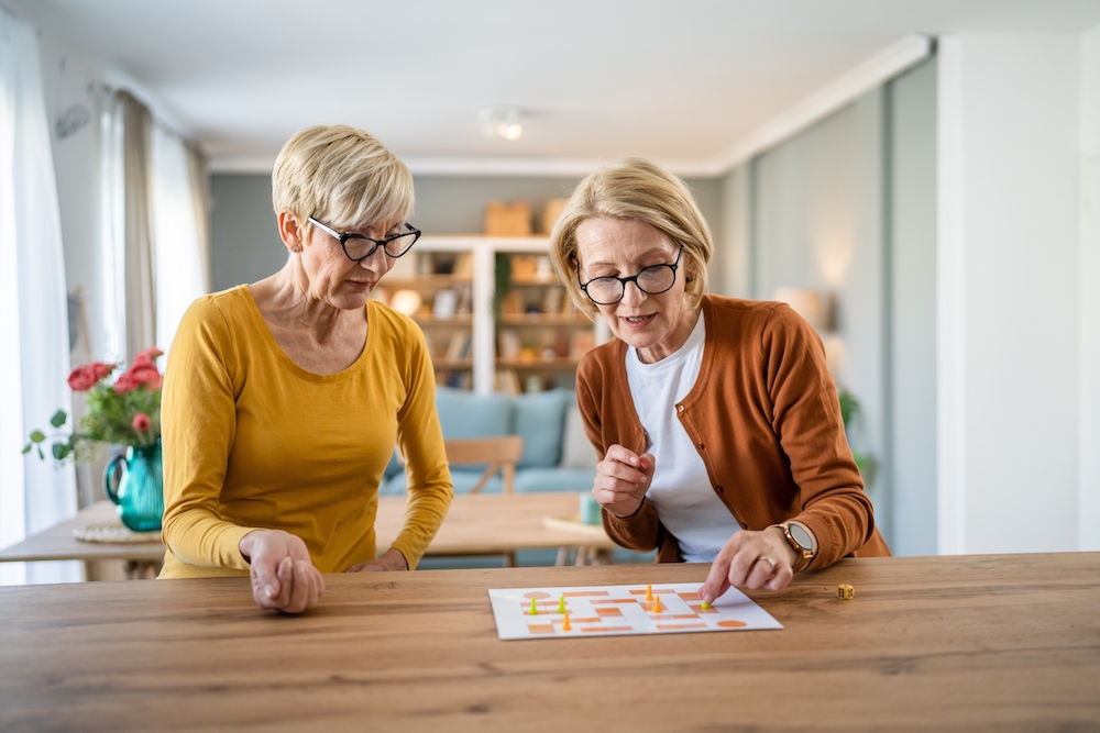 Two happy senior women play a board game while sitting at a kitchen table